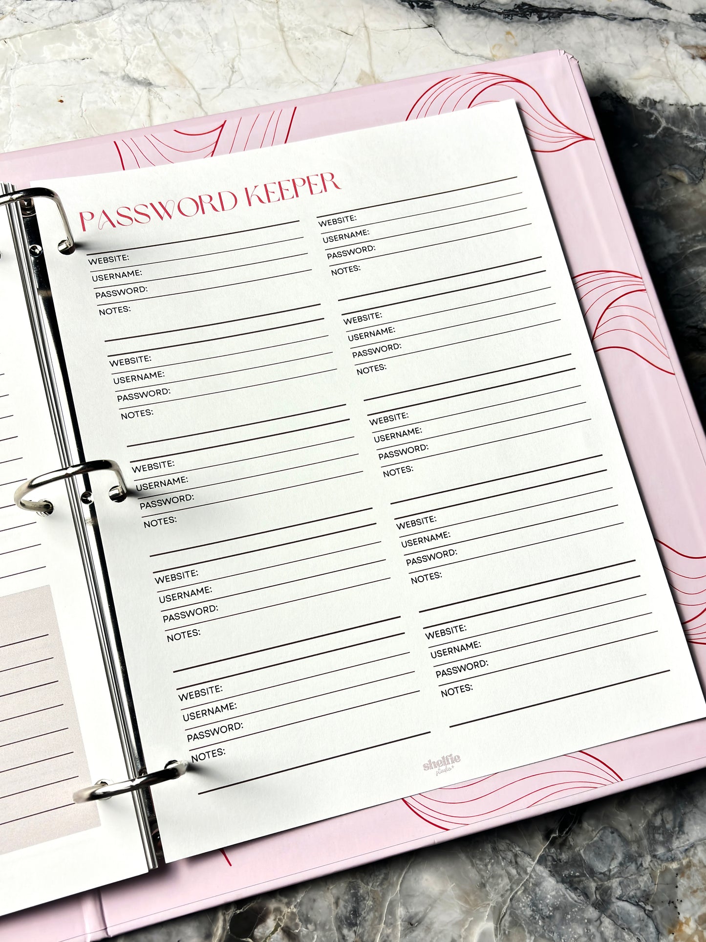 Password Keeper page in a planner with pink cover on a marble surface