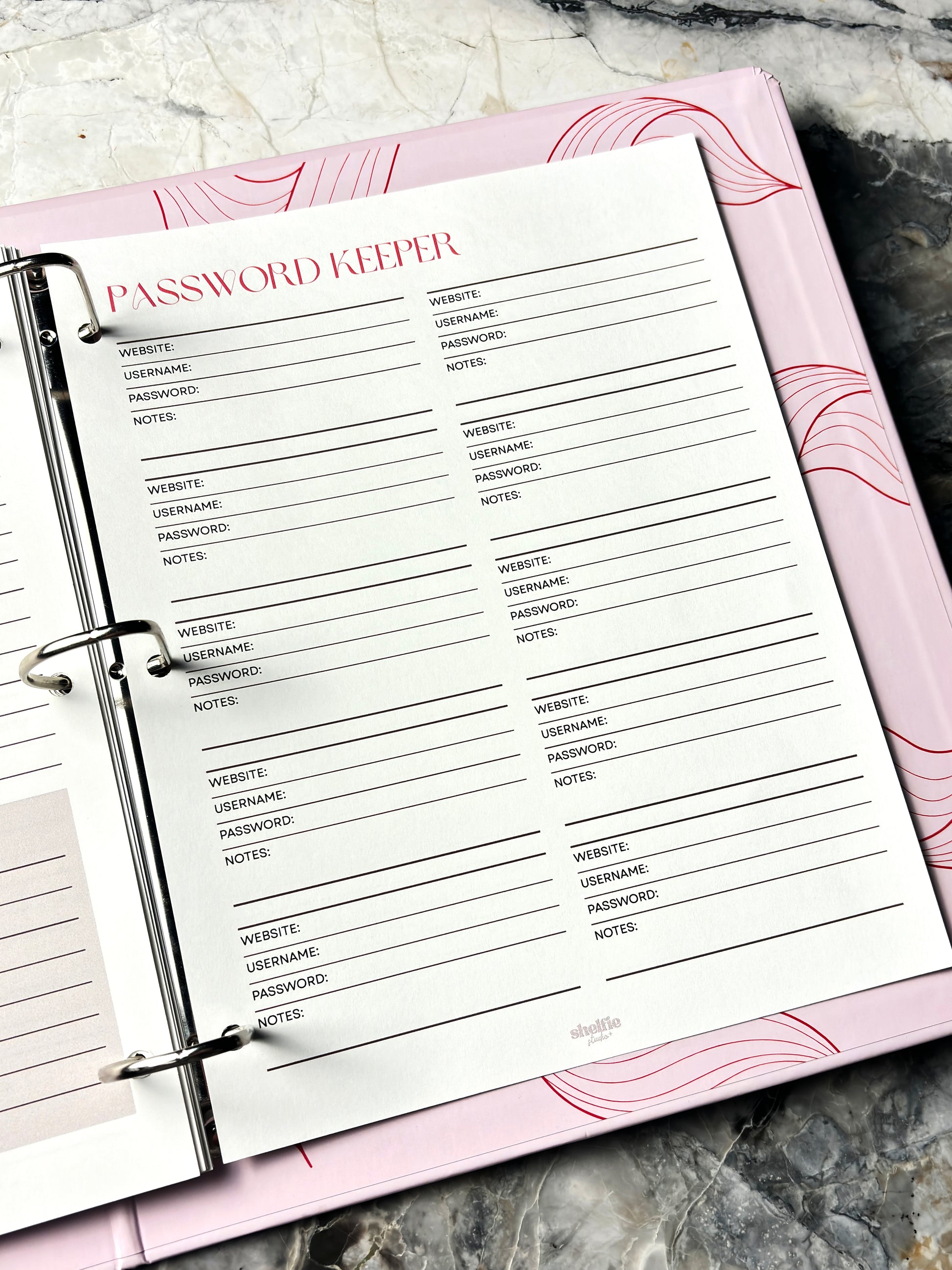 Password Keeper page in a planner with pink cover on a marble surface