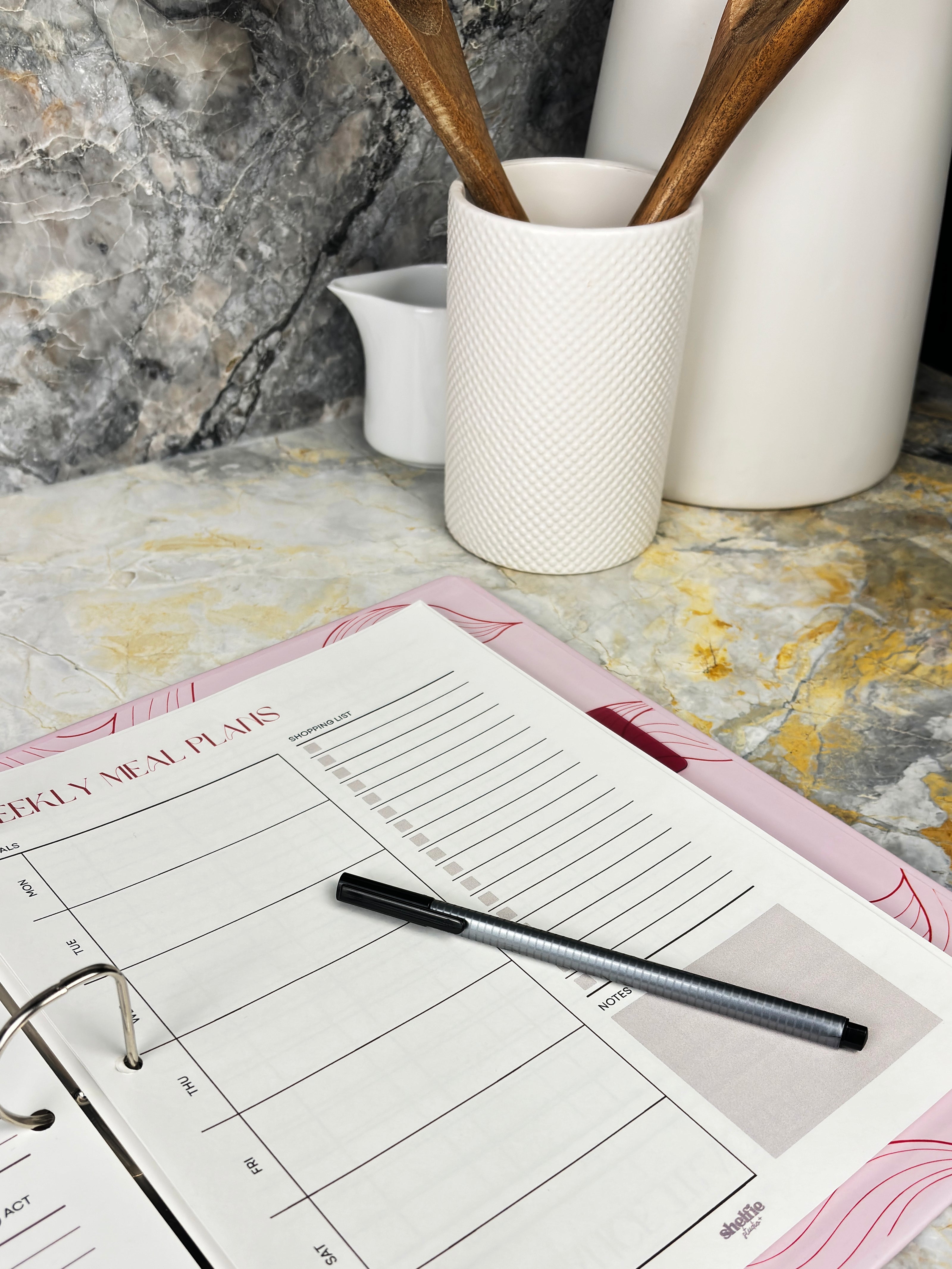 Weekly meal planner on a kitchen counter with utensils in the background