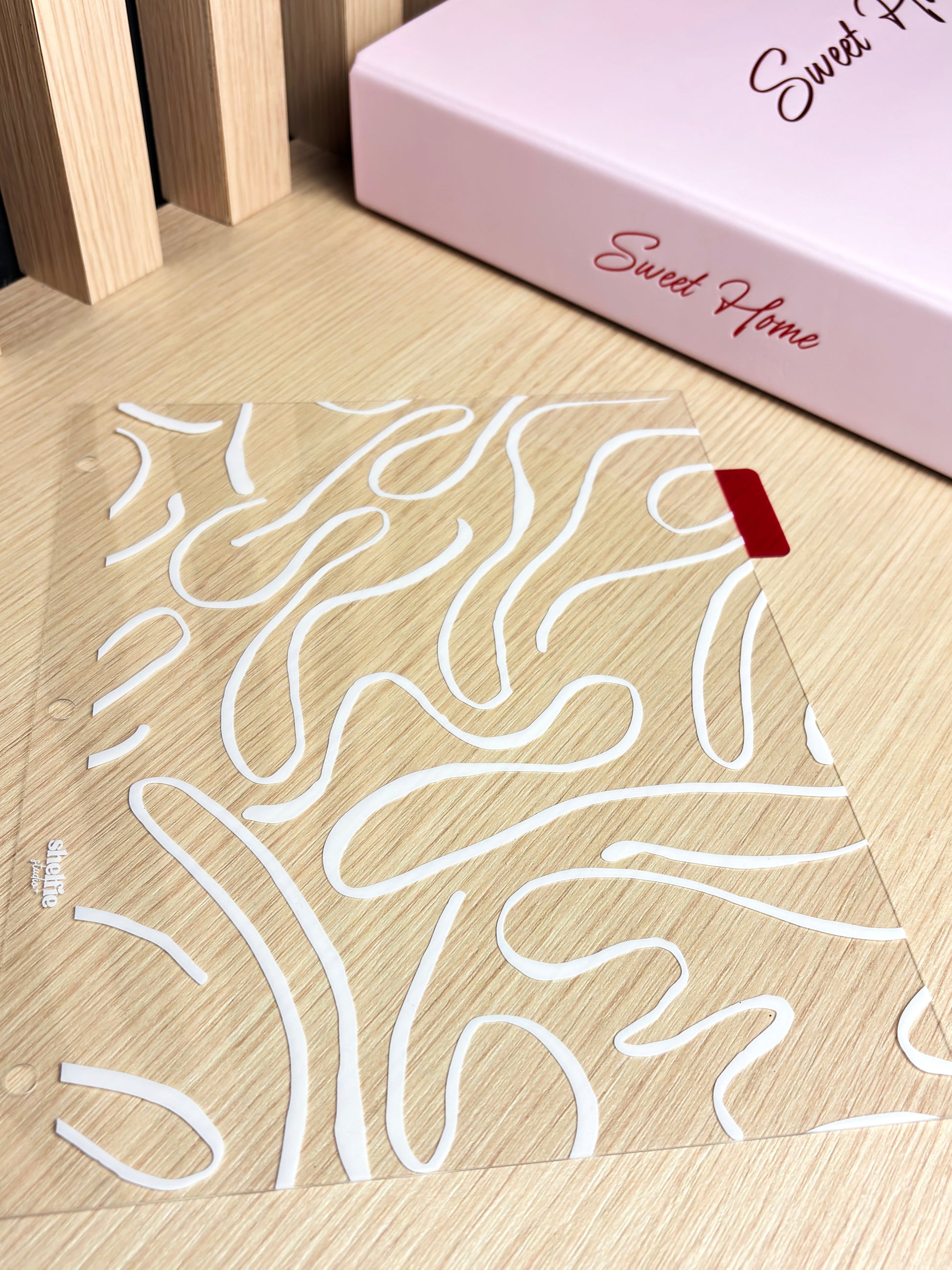 Clear acrylic sheet with white wavy line design on a wooden surface